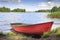 Red boat on shore on background of picturesque landscape of lake and green nature around in bright sunny summer day