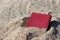 Red book on the sand on a blurry background, covered with sand, buried in the sand.