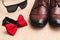 Red bow tie, brown leather men`s shoes and sunglasses on on a light fabric surface