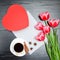 Red box in heart shaped, pink tulips, gray sheet and a coffee mu