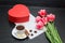 Red box in heart shaped, pink tulips, gray sheet and a coffee mu