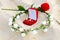 Red box with wedding rings in the center of a wreath of white flowers on the sand and a small rose in the background.