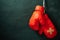 Red boxing gloves hung on black cement wall in darkness with lighting. Adhesive plaster across each other on boxing gloves. Idea