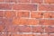 Red brick masonry wall with light cement layer, uneven and beaten surface of bricks, bright background