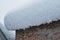 The red brick wall of the house and the huge snowdrift on the roof. In the background is a gray sky with large flakes of