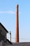 Red bricks tall industrial chimney with metal stairs and lightning rods on top rising above abandoned factory building