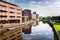 Red Brik Buildings alongside a River and Blue Sky with Clouds