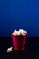 Red bucket full of popcorn on dark blue background.