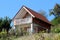 Red building blocks narrow vineyard cottage with white front balcony surrounded with densely planted vineyard and uncut grass