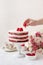 Red cake with raspberries,  white cream  and red jelly. Birthday Cake.  A woman decorates a raspberry cake for her birthday.