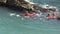 Red canoes paddling in the sea through a gap in some rocks.