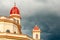 Red caped towers of basilica in honour of Our Lady of Charity with black thunder clouds above, El Cobre, Santiago de Cuba, Cuba