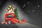 Red car on black background, headlights on. Its snowing. Christmas tree, present boxes, balloons, snow globe nearby