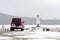 Red car in front of lighthouse on the seacoast at snowy winter day