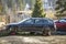 Red car parked in recreation zone and old rusty broken trash car after crash accident without wheels on wood stamps on sunny day