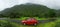 Red car parked on the road beside a mountain on a rainy day