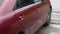 A red car is standing outside in the rain. There are many drops on the body of the car. The camera moves from left to