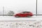 Red car, station wagon driving fast on the road in winter landscape, with snowy weather. Motion blur
