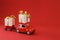 Red car with trailer delivering gifts on red background. Delivery transport concept. holiday celebration. Copy space