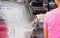 Red car washed in self serve carwash, view from rear of young woman spraying foam from high pressure hose, detail on small white