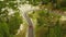 Red car winds along curvy road on highland slopes with coniferous forests. Aerial view showcases scenic serpentine