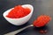 Red caviar in a white plate with a spoon lies on a black background