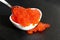 Red caviar in a white plate with a spoon lies on a black background