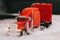 A red celebratory toy truck with a trailer shines headlights ahead. The tractor rides in the snow. Christmas holidays are coming.