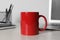 Red ceramic mug, laptop and stationery on white table at workspace