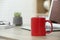 Red ceramic mug and laptop on wooden table indoors. Space for text