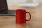 Red ceramic mug and laptop on wooden table at workplace