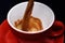 Red ceramic mug pouring, filling with coffee, sackcloth background.