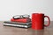 Red ceramic mug, stationery and glasses on wooden table