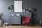 Red chair next to grey cabinet in living room interior with mock