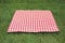 Red checkered gingham cloth on green grass. Picnic towel.Tabletop advertisement design. Food promotion display