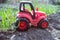 Red child tractor side view among fresh onion shoots on the field