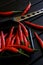 Red chilli pods and a knife for cheese and vegetables lie on a black wooden surface. Daylight. Vertical image