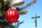 Red Christmas ball on real live outdoor Christmas tree with semi-transparent crucifix
