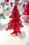 Red Christmas tree foam model decorated with little tinsel garland standing on shelf and shade of light.