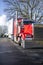 Red classic big rig semi truck tractor with chrome accessories and dry van semi trailer standing on the city street parking in