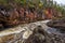 Red cliff, stone wall, forest, waterfall and wild river view in autumn