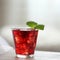 Red cocktail with ice, decorated with mint leaf on light background