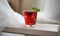 Red cocktail with ice, decorated with mint leaf on light background