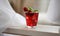 Red cocktail with ice, decorated with mint leaf, lime and trawberry on light background