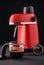 A red coffee machine with chrome parts and a glass pitcher and portafilter with ground coffee grains on a dark background. Still-