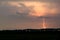 Red colored lightning bolt strikes from a distant thunderstorm