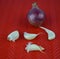 A red colored medium sized fresh onion and some scattered garlic seed