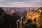 Red colors on the rock cliff faces of the Grand Canyon during sunset with a tree standing on the edge