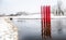 Red colour structure of four set of parallel poles erected in the centre of a lake. Season is Winter with lot of white snow.