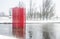 Red colour structure of four set of parallel poles erected in the centre of a lake. Season is Winter with lot of white snow.